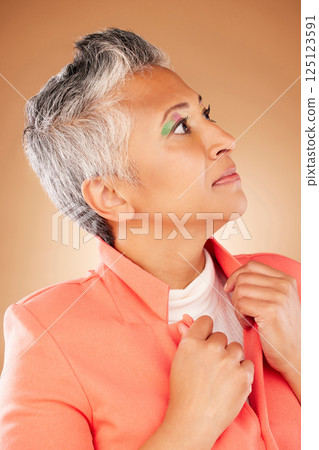 Thinking, fashion and senior woman with makeup, designer style and elegant with clothes against a brown studio background. Cosmetics, face and elderly stylish model with idea about for clothing 125123591