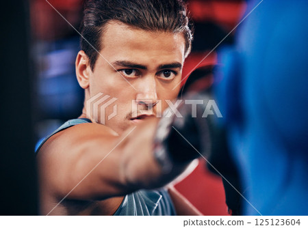 Fitness, boxing and athlete training at a gym for a fighting match with a punching bag and gloves. Motivation, martial arts and man boxer or fighter practicing for MMA competition at a sports center. 125123604