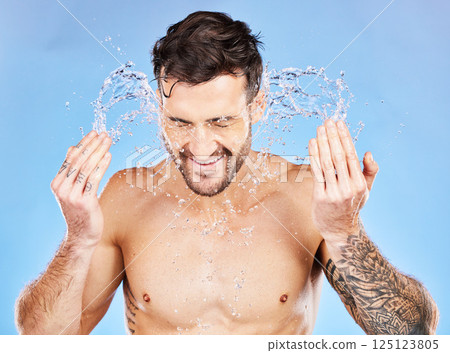 Grooming, splash and man washing face with water for cleaning, hygiene and wellness against a blue studio background. Skincare, beauty and model with a facial water splash for body in the morning 125123805