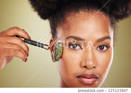 Skincare, beauty and black woman with face roller, facial massage for glowing healthy skin. Wellness, dermatology and relax, portrait of woman with jade roller for anti aging treatment in studio 125123807