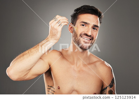 Skincare, face and man apply serum for skin care, glowing and healthy skin on a grey studio background. Treatment, facial hyaluronic acid and natural oil portrait for clean and fresh skin 125123914