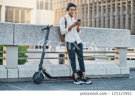 Phone, music and electric scooter with a business black man streaming audio during his commute into work. Mobile, headphones and transport with a male employee typing a text message in an urban town Phone, music and electric scooter with a business black man streaming audio during his commute into work. Mobile, headphones and transport with a male employee typing a text message in an urban town 125123981