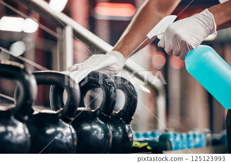 Kettlebell, cleaning service and hands cleaning at a gym with liquid soap in spray bottle with cloth in gloves. Janitor or cleaner wipes dirty bacteria on dusty weights or fitness training equipment 125123993