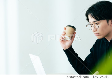 Young man looking at computer while drinking coffee 125125010