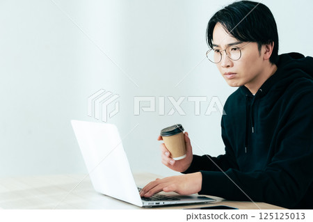 Young man looking at computer while drinking coffee 125125013