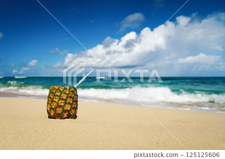 Pineapple  cup with a straw in it on the sand  with the ocean in the background. Summer vacation 125125606