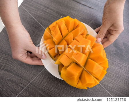 Half cutted cubes slices ripe mango on white plate in hands Half cutted cubes slices ripe mango on white plate in hands 125125758