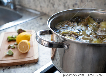 Cleaned artichokes preparing in metal pan on cooker, artichoke cooking process at kitchen interior Cleaned artichokes preparing in metal pan on cooker, artichoke cooking process at kitchen interior 125125766