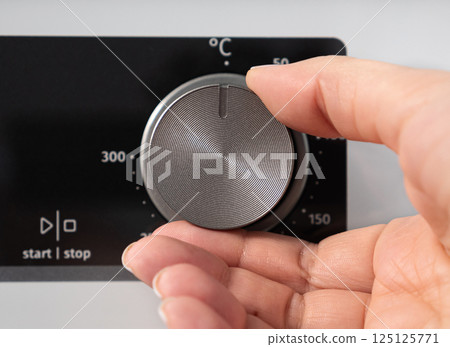 Woman adjusting modern white oven in kitchen.  Female hand pushing and turning knobs on oven control panel 125125771