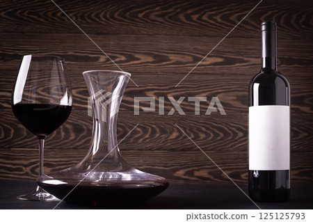 Decanter, glass and bottle with red wine on wooden rustic background 125125793