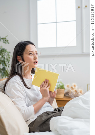 Woman with glasses thinking while looking at her notebook indoors | Diary reading | Healthy living image | Well-being girl | Well-being 125125917