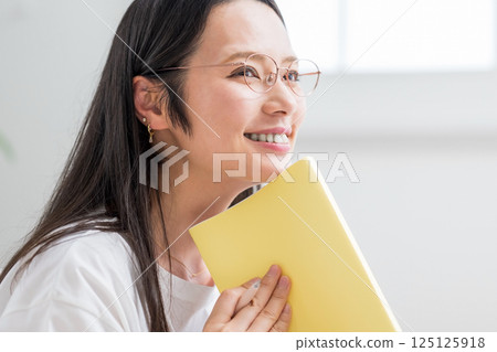 Smiling woman with glasses looking at her notebook indoors | Diary reading | Healthy living image | Well-being girl | Well-being 125125918