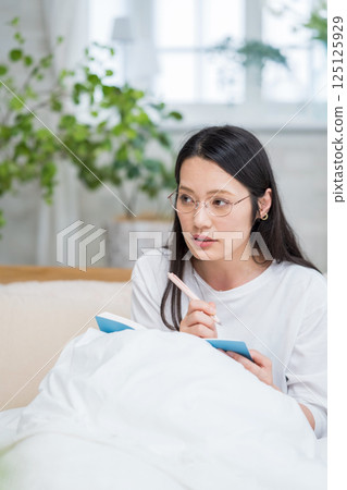 戴眼鏡的女人在床上看著筆記本思考日記 |健康生活方式圖像 |幸福女孩 |福利 125125929