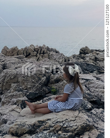 A child by the ocean on a rocky shoreline, enjoying nature and adventure in a summer breeze 125127100