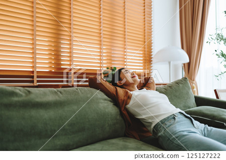 Relaxed young Asian woman enjoying rest on comfortable sofa 125127222
