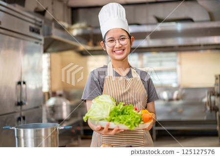 Smiling Young Chef Presenting Fresh Vegetables in Kitchen Smiling Young Chef Presenting Fresh Vegetables in Kitchen 125127576