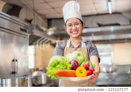 Smiling Young Chef Presenting Fresh Vegetables in Kitchen Smiling Young Chef Presenting Fresh Vegetables in Kitchen 125127577