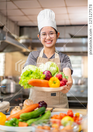 Smiling Young Chef Presenting Fresh Vegetables in Kitchen 125127578