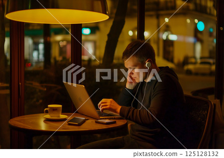 晚上在咖啡館遠距工作的人和一台電腦的場景 晚上在咖啡館遠距工作的人和一台電腦的場景 125128132