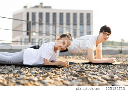 Mother and daughter practicing fitness exercises together outdoors illustrating family bonding and healthy habits. Individuals performing plank exercise in outdoor urban setting Mother and daughter practicing fitness exercises together outdoors illustrating family bonding and healthy habits. Individuals performing plank exercise in outdoor urban setting 125129713