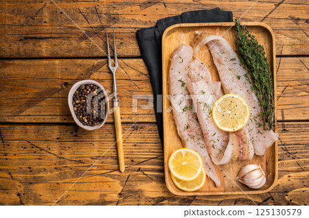 Raw Pollock and Hake fish fillets on a wooden board with herbs ready for cooking. wooden background. top view 125130579