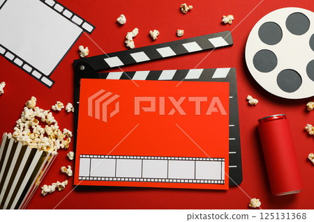 Clapperboard, paper cup with popcorn, film and reel on red background, top view 125131368