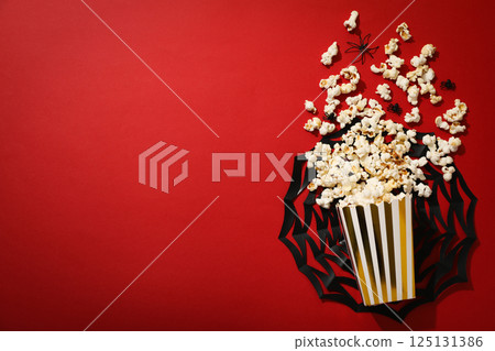 Paper cup with popcorn, spiders and paper web on red background, space for text 125131386