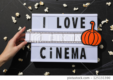 Popcorn, spider web, hand, paper pumpkin and light box with text on black background, top view Popcorn, spider web, hand, paper pumpkin and light box with text on black background, top view 125131390