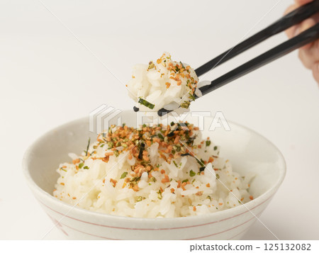 Pick up warm rice topped with salmon and seaweed sprinkles with chopsticks 125132082