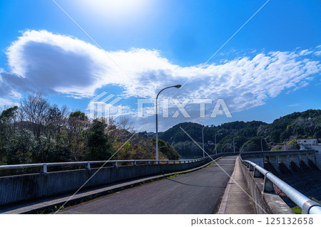 Nunome Dam in cherry blossom season: Asphalt road on the dam and cirrocumulus clouds floating in the clear sky① 125132658