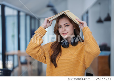 happy young woman with headphones is immersed in a book, happily learning 125133755