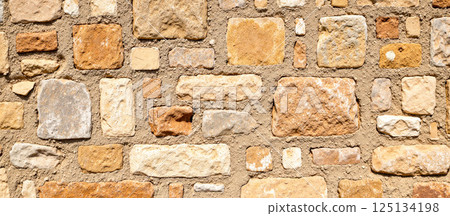 Close-up view of rough orange and yellow bricks with cement joints, aged vintage wall texture, natural stone structure background for design, restoration, construction 125134198