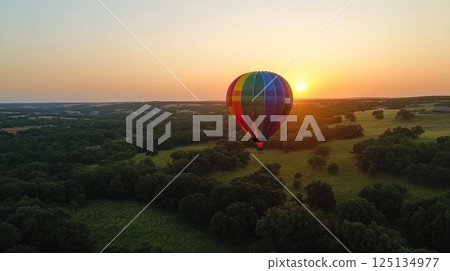 Colorful hot air balloon soaring over scenic landscape at sunset. 125134977