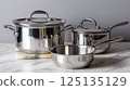Stainless steel cookware set displayed on a marble countertop in a modern kitchen 125135129