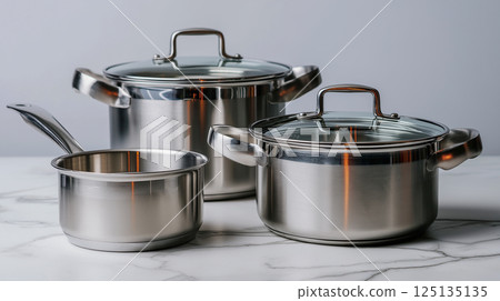 Stainless steel pot and pan set arranged on marble countertop in well-lit kitchen 125135135