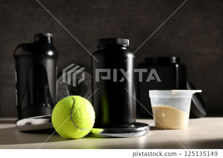 Black plastic jars and bottle, measuring cup and sport equipment on dark gray background Black plastic jars and bottle, measuring cup and sport equipment on dark gray background 125135149