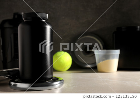 Black plastic jars and bottle, measuring cup and sport equipment on dark gray background, space for text 125135150