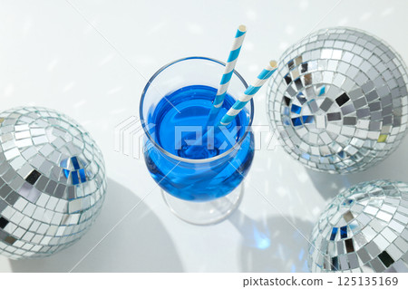 Blue cocktail with straws in glass and disco balls on white background, top view 125135169