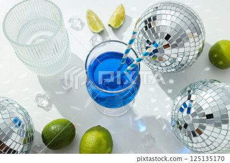 Blue cocktail in glass, limes, ice cubes and disco balls on white background, top view 125135170