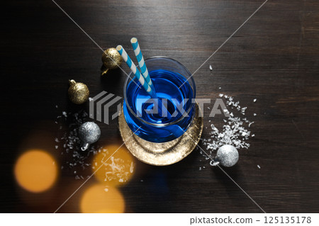Blue cocktail with straws in glass, snow and balls on wooden background, top view Blue cocktail with straws in glass, snow and balls on wooden background, top view 125135178