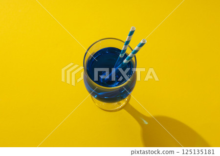 Blue cocktail with straws in glass on yellow background, top view Blue cocktail with straws in glass on yellow background, top view 125135181