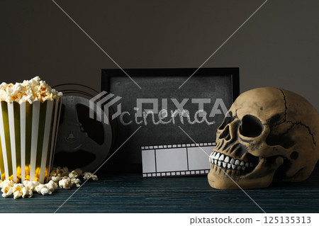 Blackboard, skull, reel and paper cup with popcorn on dark background Blackboard, skull, reel and paper cup with popcorn on dark background 125135313