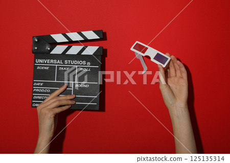 Clapperboard and 3D glasses in hands on red background Clapperboard and 3D glasses in hands on red background 125135314