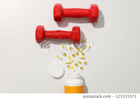 Plastic jar with vitamins and red dumbbells on white background, top view Plastic jar with vitamins and red dumbbells on white background, top view 125135371