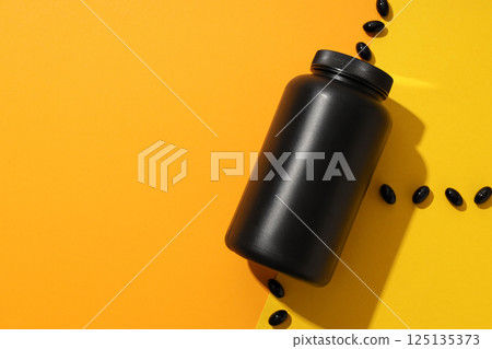 Black plastic jar with pills on yellow background, space for text 125135373