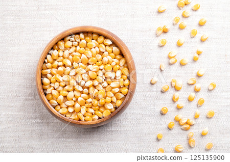Unpopped popcorn kernels in a wooden bowl on linen. Seeds of Zea mays variety everta, rounded at the top, which expand and puffs up, when heated. Snack food, sometimes sold as pearls, or as old maids. 125135900