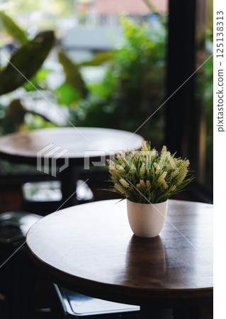 A potted plant sits on a wooden table in a restaurant. The plant is green and he is a fake A potted plant sits on a wooden table in a restaurant. The plant is green and he is a fake 125138313