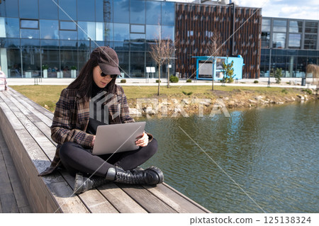 Woman Using Laptop by Pond in Urban Setting Woman Using Laptop by Pond in Urban Setting 125138324