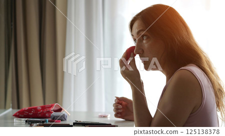 Woman applying foundation on face in hotel room Woman applying foundation on face in hotel room 125138378