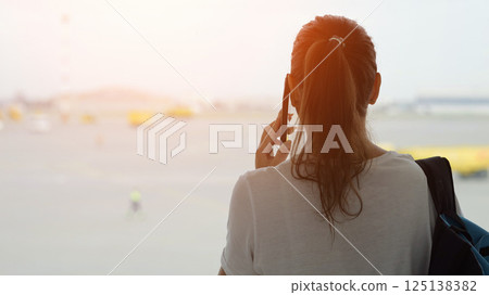 Lady calls on phone looking out window at aircraft movement area 125138382